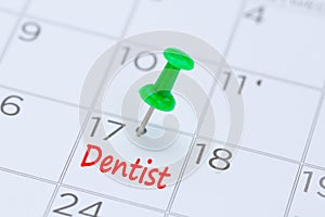Dentist written on a calendar with a green push pin to remind y