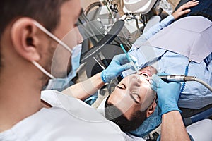 Dentistry dedicated to excellence. Dentist in latex gloves examining male patient, lying in dental chair with opened