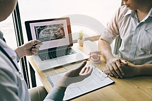 Dentists are discussing dental problems at report x-ray image on laptop screen to patients