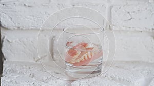 A denture in a glass of water. Dental prosthesis care. Full removable plastic denture of the jaws.