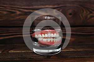 A denture in a glass of water. Dental prosthesis care. Full removable plastic denture of the jaws. Two acrylic dentures.