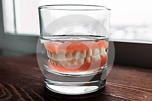 A denture in a glass of water. Dental prosthesis care. Full removable plastic denture of the jaws. Two acrylic dentures.