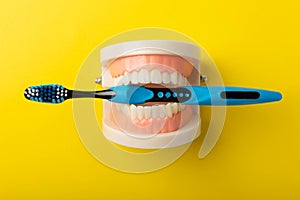 Dentures with a blue toothbrush on a yellow background.