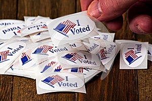 Denver, CO--June 30; hand reaching into pile of red white and blue oval I Voted sticker to take one and place on clothes after