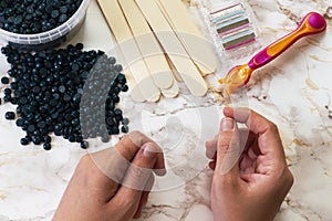 Depilatory pearly blue solid wax beans and wooden stick, disposable razors on marble background