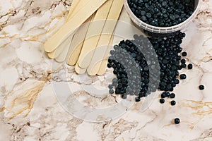 Depilatory pearly blue solid wax beans and wooden stick on marble background