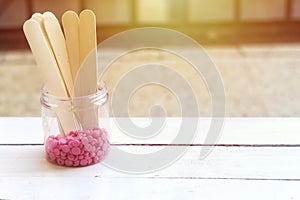 Depilatory pearly pink solid wax beans and wooden stick wood on wood background