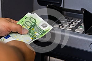 Depositor withdraws EURO from ATM cash money machine. Man hand holding EURO banknotes at the ATM machine photo