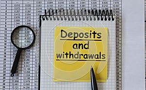 DEPOSITS and withdrawals - words in a white notebook on the background of a table with numbers and a magnifying glass photo