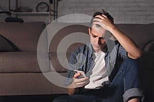 Deppresed teen guy checking mobile phone in dark room