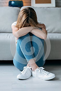 Depresive young woman thinking about her problems while sitting on the floor in the living room at home