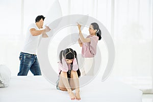 Depress asian girl child cover her ears with parents having argument using pillow fight together in the background