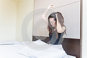 Depress woman sitting on bed in room hitting a pillow