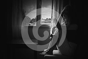 depress woman sitting on chair in room near window in white tone