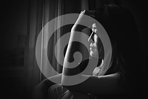 depress woman sitting on chair in room near window in white tone