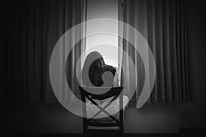 depress woman sitting on chair in room near window in white tone,