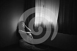 Depress woman sitting on floor in room near window in white tone
