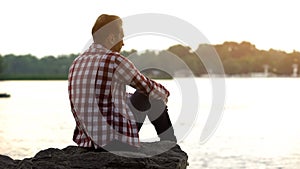 Depressed adult male sitting on riverside and thinking about divorce, loneliness