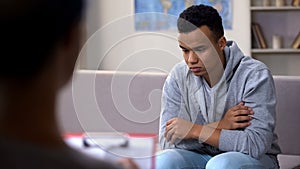 Depressed African-American teenager talking to psychologist, racism at school