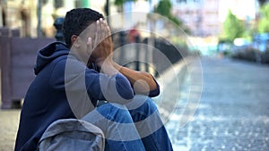 Depressed Afro-American male teenager sitting on city street, escape from home