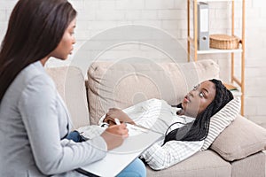 Depressed afro woman discussing her problems with psychotherapist at personal consultation