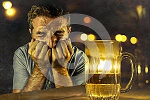 Depressed alcoholic man drinking beer wasted and drunk failing resisting to drink in bar pub at night falling into alcohol abuse