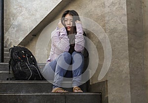 Depressed Asian American student woman or bullied teenager sitting outdoors on street staircase overwhelmed and anxious feeling