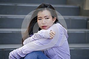 Depressed Asian American student woman or bullied teenager sitting outdoors on street staircase overwhelmed and anxious feeling