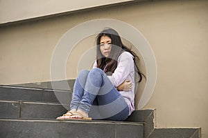 Depressed Asian Chinese student woman or bullied teenager sitting outdoors on street staircase overwhelmed and anxious feeling