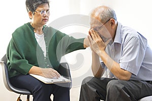 Depressed Asian senior man sharing problems during therapy session with female psychiatrist