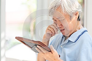 Depressed asian senior woman holding a picture frame and watching old photographs of family at home,devastated elderly people