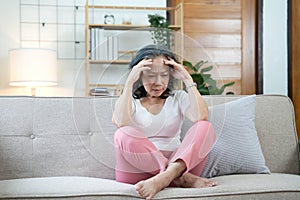 Depressed Asian senior woman sit on sofa looking away by the window. Loneliness elderly female living alone at home with