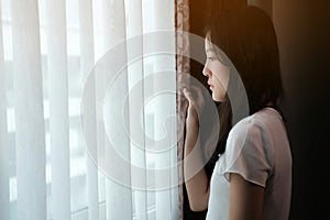 A depressed Asian woman stands at the window