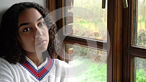 Depressed beautiful mixed race African American girl teenager young woman sitting looking out of a window