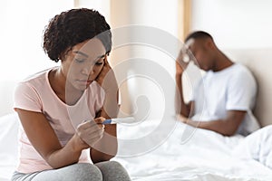 Depressed black woman holding pregnancy test, unintended pregnancy concept photo