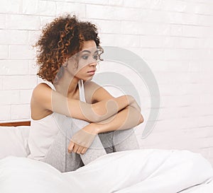 Depressed black woman sitting in bed and thinking about her problems