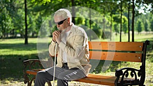 Depressed blind man sitting alone in park, socially disadvantaged population