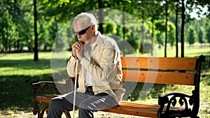 Depressed blind man sitting alone in park, socially disadvantaged population