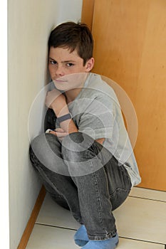 Depressed boy hidden in the corner of a room