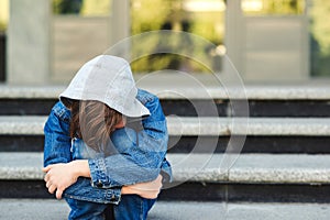 Depressed boy sitting alone with sad feeling outside school. Schoolboy sits at stairs and crying. School bullying concept