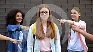 Depressed bullying victim eyeglasses looking camera, teenagers pointing fingers