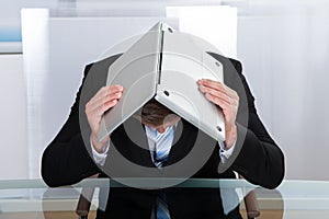Depressed businessman hiding under his laptop