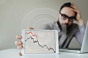 Depressed businessman leaning head below bad stock market chart