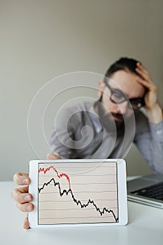 Depressed businessman leaning head below bad stock market chart