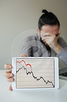 Depressed businessman leaning head below bad stock market chart