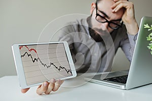 Depressed businessman leaning head below bad stock market chart