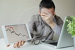 Depressed businessman leaning head below bad stock market chart