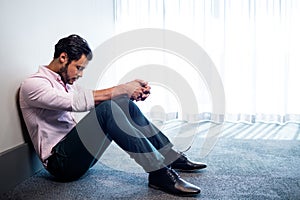 Depressed businessman sitting against a wall and looking down