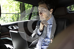 Depressed businessman sitting on backseat of his luxury car and feeling bad