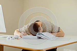 Depressed caucasian man with headache sitting at his desk in the office. Stressed young employee has problems at work